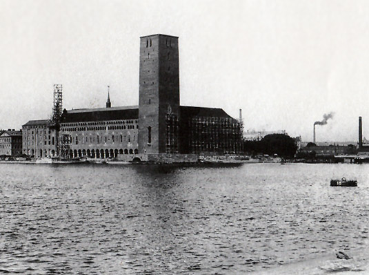 Stadshuset har blivit själva symbolen för Stockholm fastän de tre kronorna på tornets spets egentligen är staten Sveriges riksvapen. Ännu var nyfikenheten stor 1919 när bilden togs om hur tornet skulle komma att se ut. Bygget hade pågått i över ett decennium redan. Observera fabriksskorstenarna! Staden var fortfarande en industristad. Det rådde badförbud i Riddarfjärden, vattnet var förgiftat av industriföroreningar.